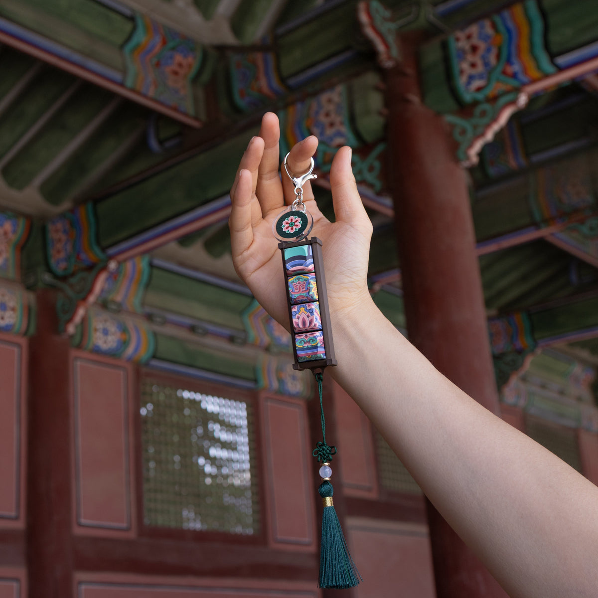 Hand holding a Black Dancheong keycap keychain beside a palace pillar