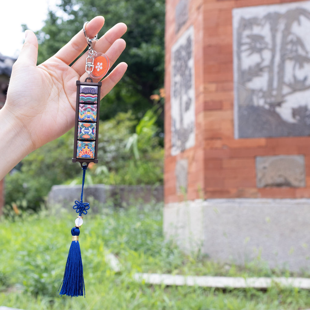 Hand holding a Gyotaejeon Dancheong keycap keychain beside a palace pillar
