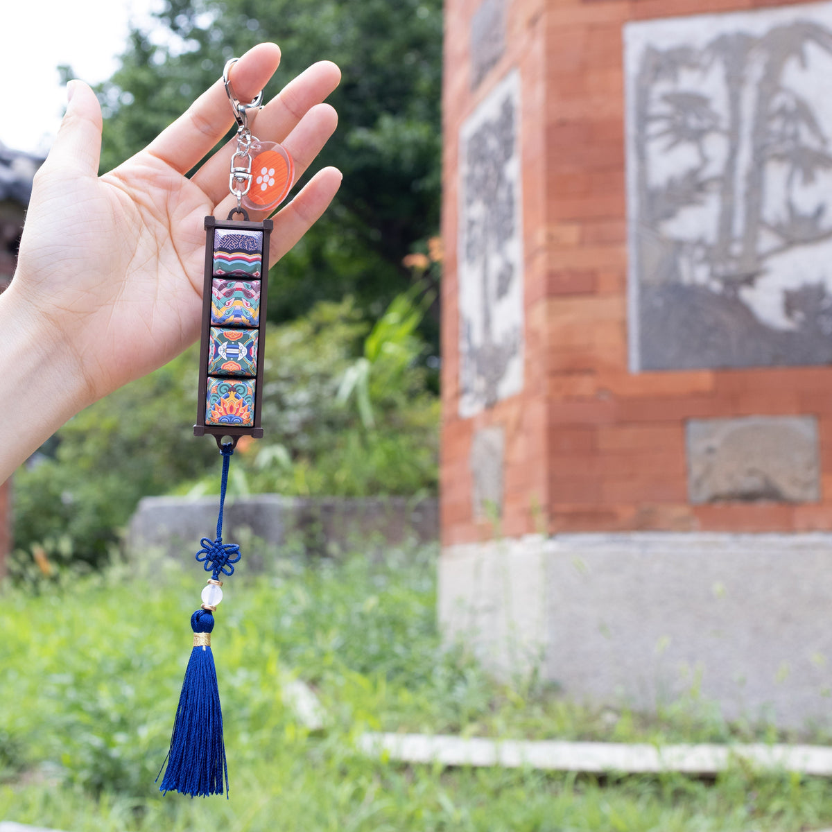Hand holding a Gyotaejeon Dancheong keycap keychain beside a palace pillar